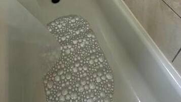 A bathtub with bubbles, a soap dish, and a showerhead.