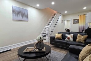 A modern living room with a staircase, a black leather sofa, and a round coffee table with decorative items. - Work-Crew & Family Stay Near I-78 - Free Parking (Reading)