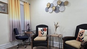Una stanza con due poltrone in vimini, un tavolino con un vaso e una scrivania con una lampada.