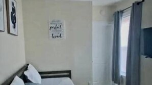 Una camera da letto con un letto, una ventola a soffitto, una finestra con tende e un muro con un cartello.