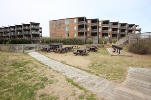 A residential building with multiple balconies, a grassy courtyard with picnic tables, and a wooden deck. - Duck, NC - Oceanfront and Unlimited Sunrises!  Welcome to Sandy Quacks! (Kitty Hawk)