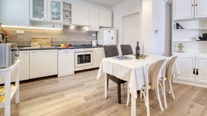 A modern kitchen with white cabinetry, a dining area with a table set for two, and a white refrigerator. - Villa Nika by Interhome (Opatija/Ika)