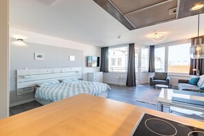 A modern hotel room with a large bed, a sofa, a dining table, and a TV. - Sandbank Domizil in Haus Seeblick - view of the North Sea! - Lake view (Borkum)