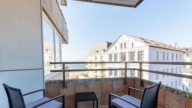 Un balcon avec deux chaises et une petite table, d’où l’on peut admirer un panorama sur la ville, avec ses bâtiments historiques.