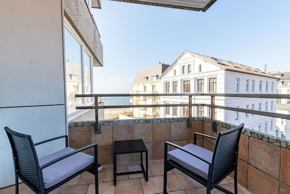 A balcony with two chairs and a small table, overlooking a cityscape with historic buildings.