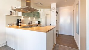 Une cuisine moderne dotée d’un îlot central, d’une hotte en acier inoxydable et d’appareils électroménagers intégrés.
