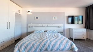 Une chambre moderne avec un lit, une armoire blanche et un téléviseur à écran plat.