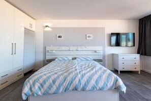 A modern bedroom with a bed, white wardrobe, and a flat-screen TV.