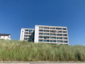 Un immeuble à plusieurs étages, orné d’un logo bien visible sur le côté, et entouré d’herbes hautes.