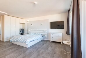 Een moderne slaapkamer met een bed, kast, televisie en een klein nachtkastje.