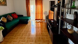 A living room with a green sofa, a TV, and a wooden floor.