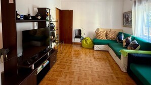 A living room with a TV, wooden flooring, a green sofa, and a hanging lamp.