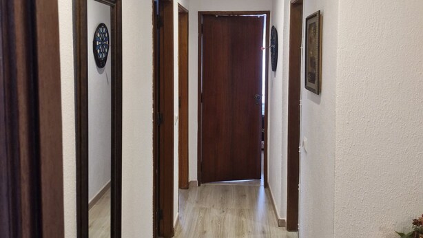 A hallway with wooden doors, a dartboard, and a small wooden cabinet.