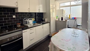 A kitchen with white cabinets, a black tiled backsplash, a stove, and a dining table with a floral tablecloth.