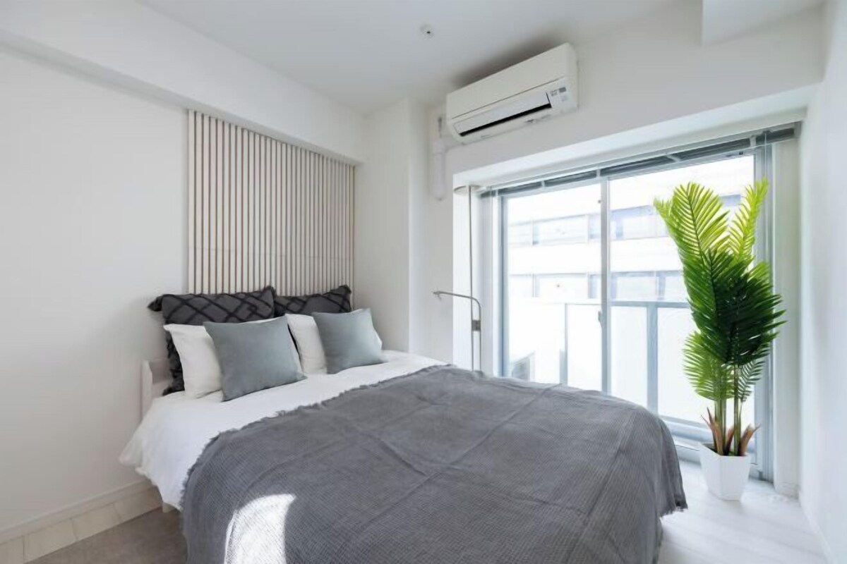 A modern bedroom with a large bed, a window with a view, and an air conditioning unit.