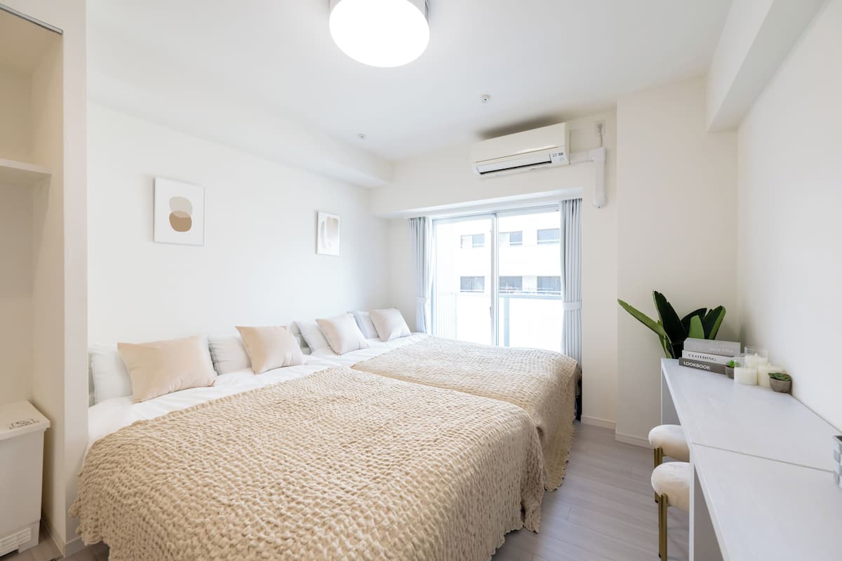 A modern bedroom with two beds, a desk, and a window.