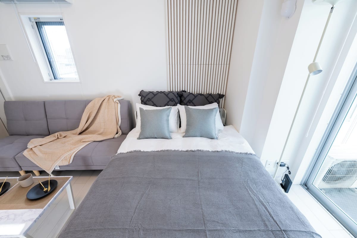 A modern bedroom with a bed, grey sofa, and a window.