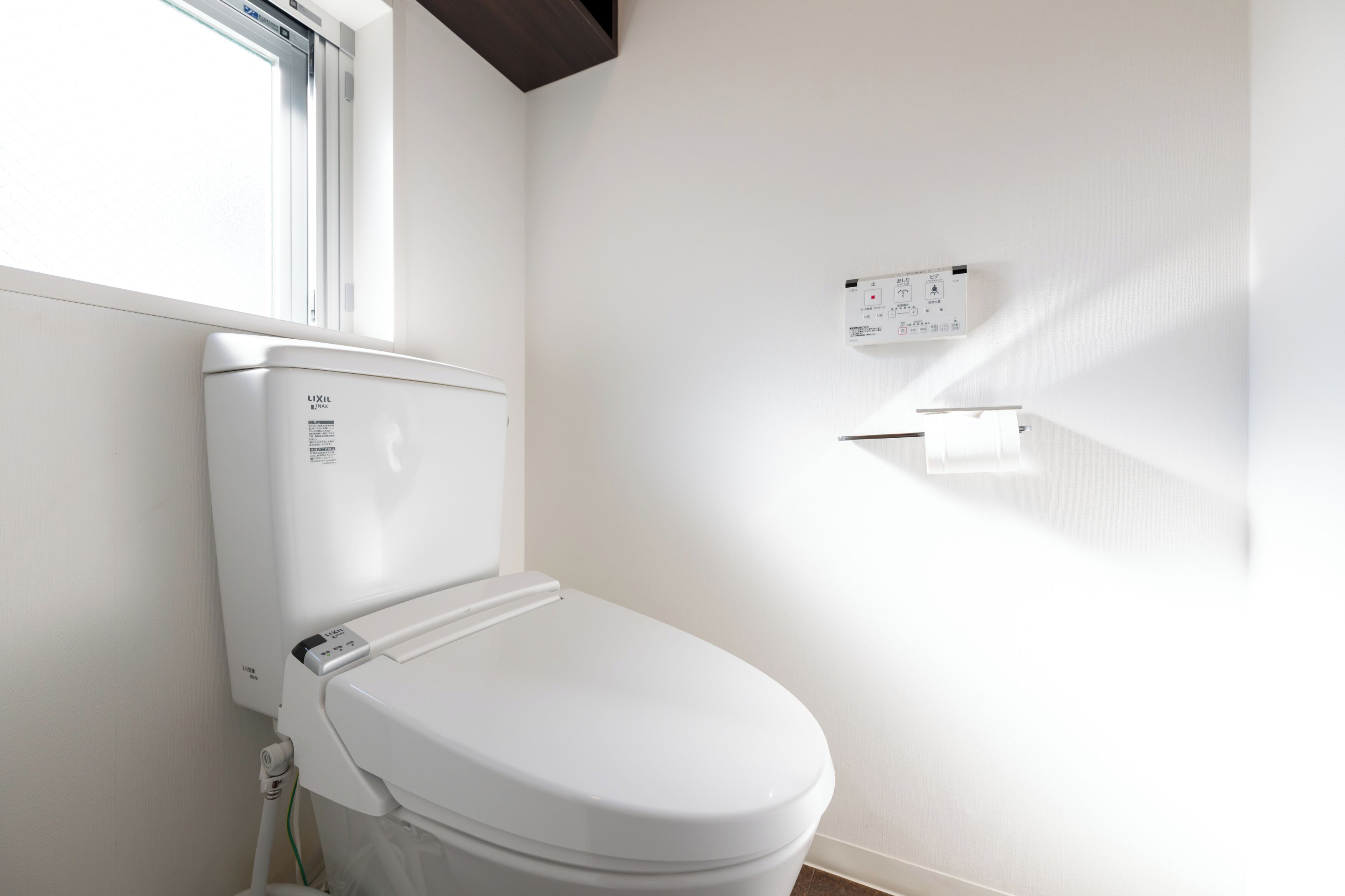 A modern bathroom with a white toilet, a visible water heater, and a control panel on the wall.
