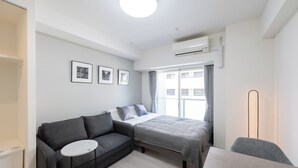 A modern, well-lit room with a bed, a gray sofa, a small round table, and a floor lamp.