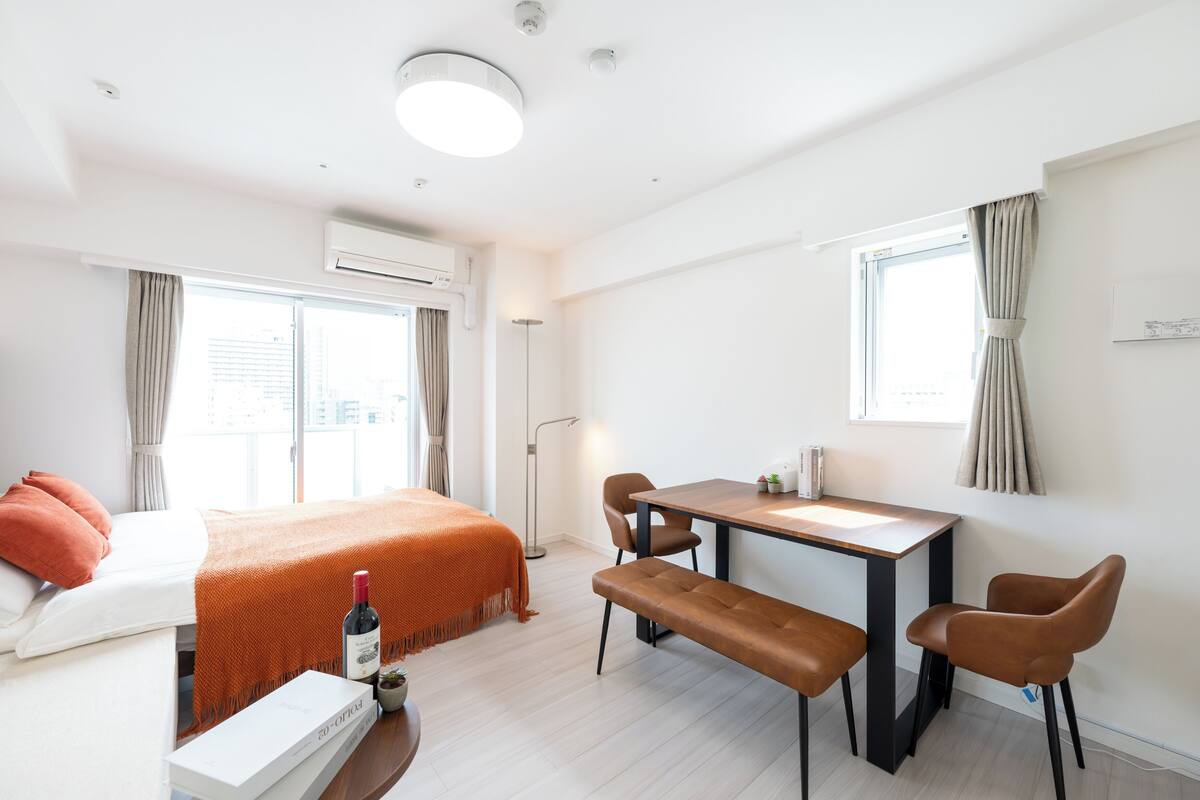A modern hotel room with a bed, a desk, a bench, and a window.