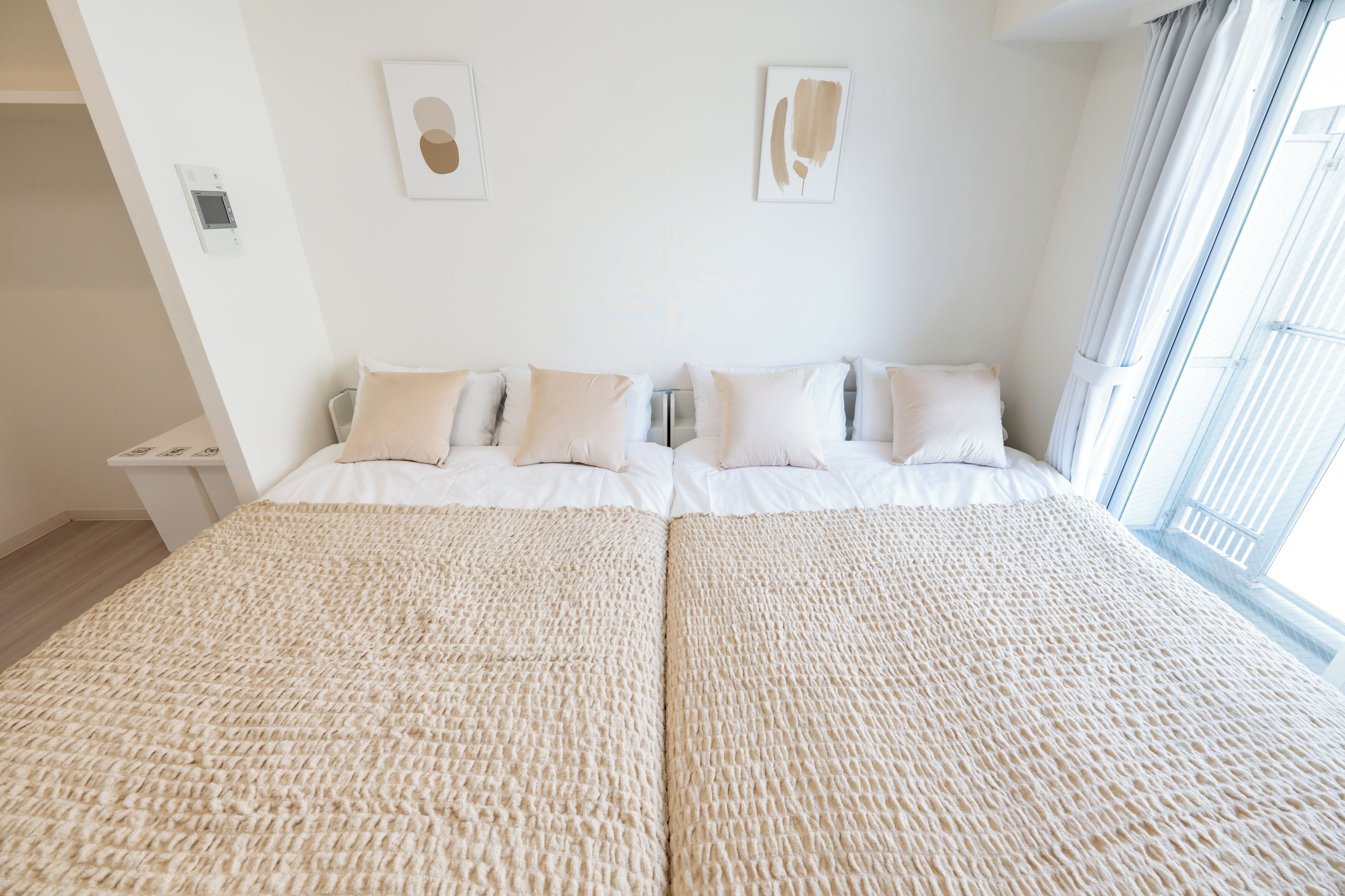 Un lit double recouvert d’une couverture beige à texture, avec une literie blanche et deux œuvres d’art accrochées au mur.