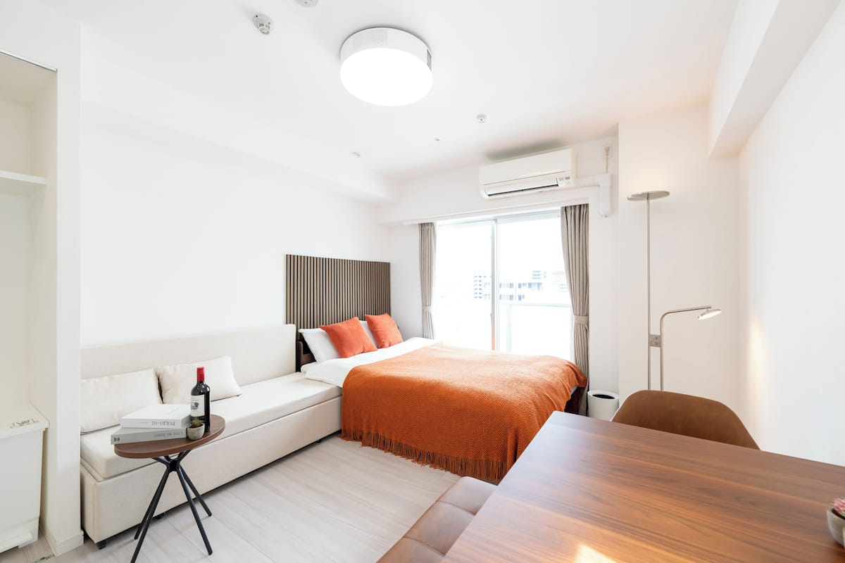 A modern hotel room with a bed, a sofa, a dining table, and a standing lamp.