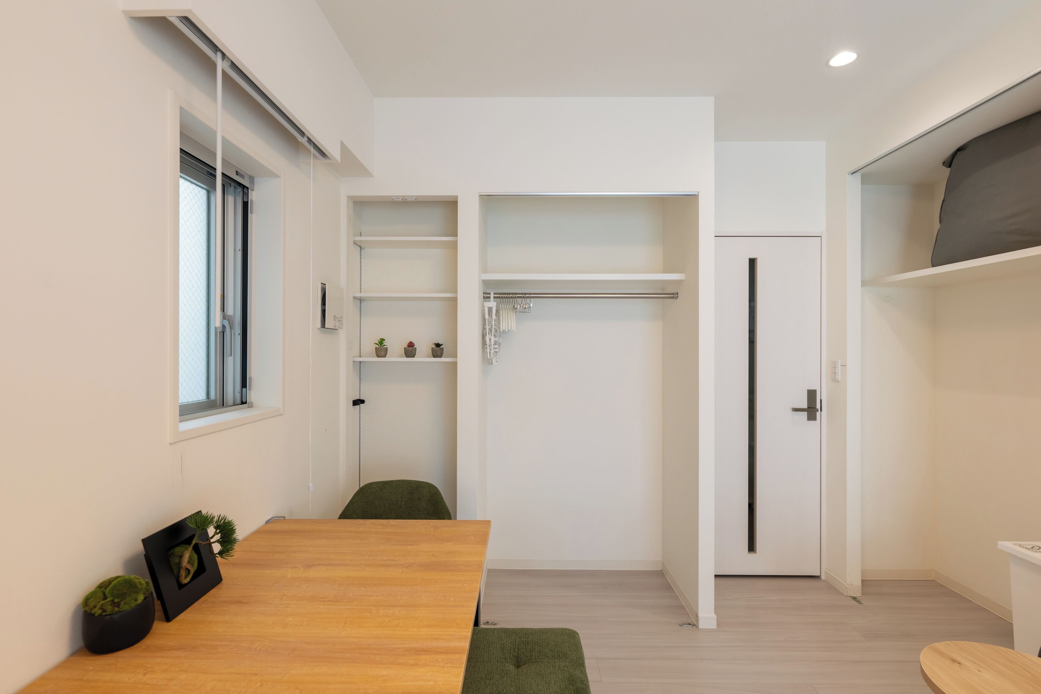 A modern, minimalist room with a wooden table, green chairs, a built-in shelf with decorative items, and a sliding door closet.