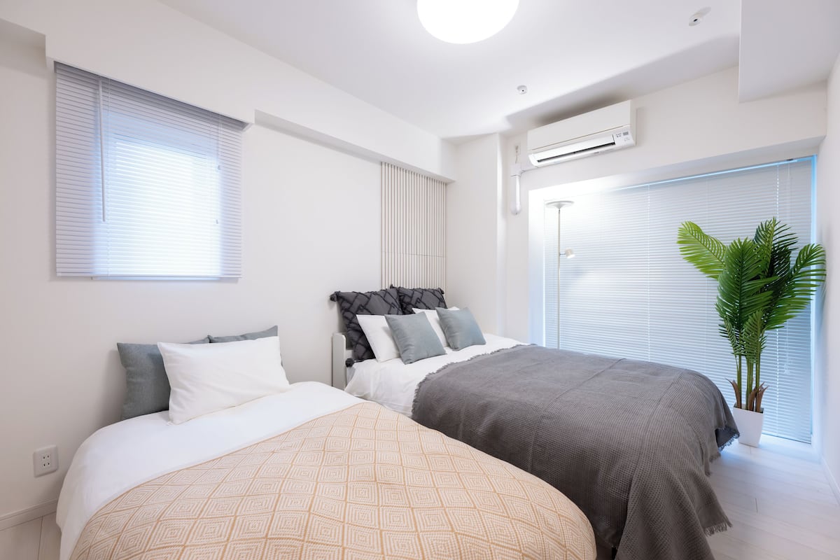 A bedroom with two beds, white walls, and a potted plant.