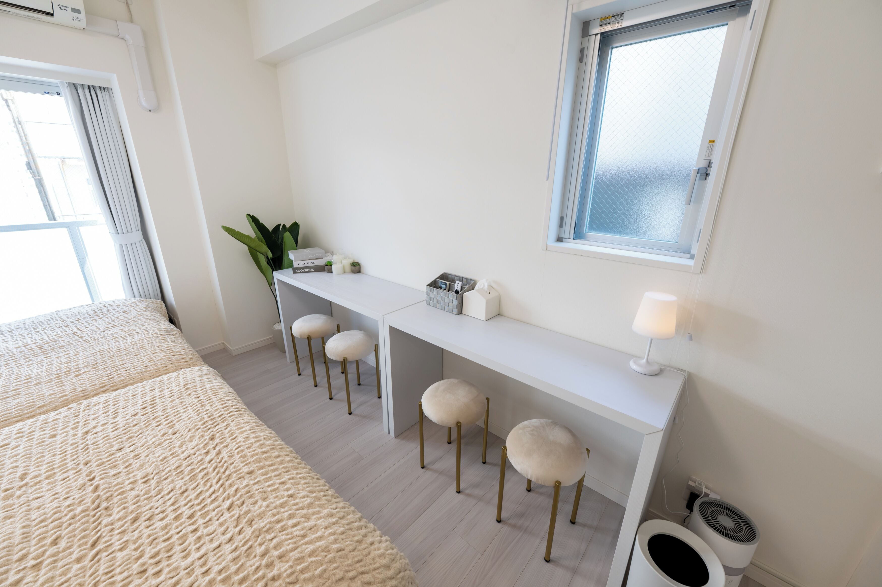Een moderne slaapkamer met een groot bed, een bureau met krukken, een kleine plant en een raam.