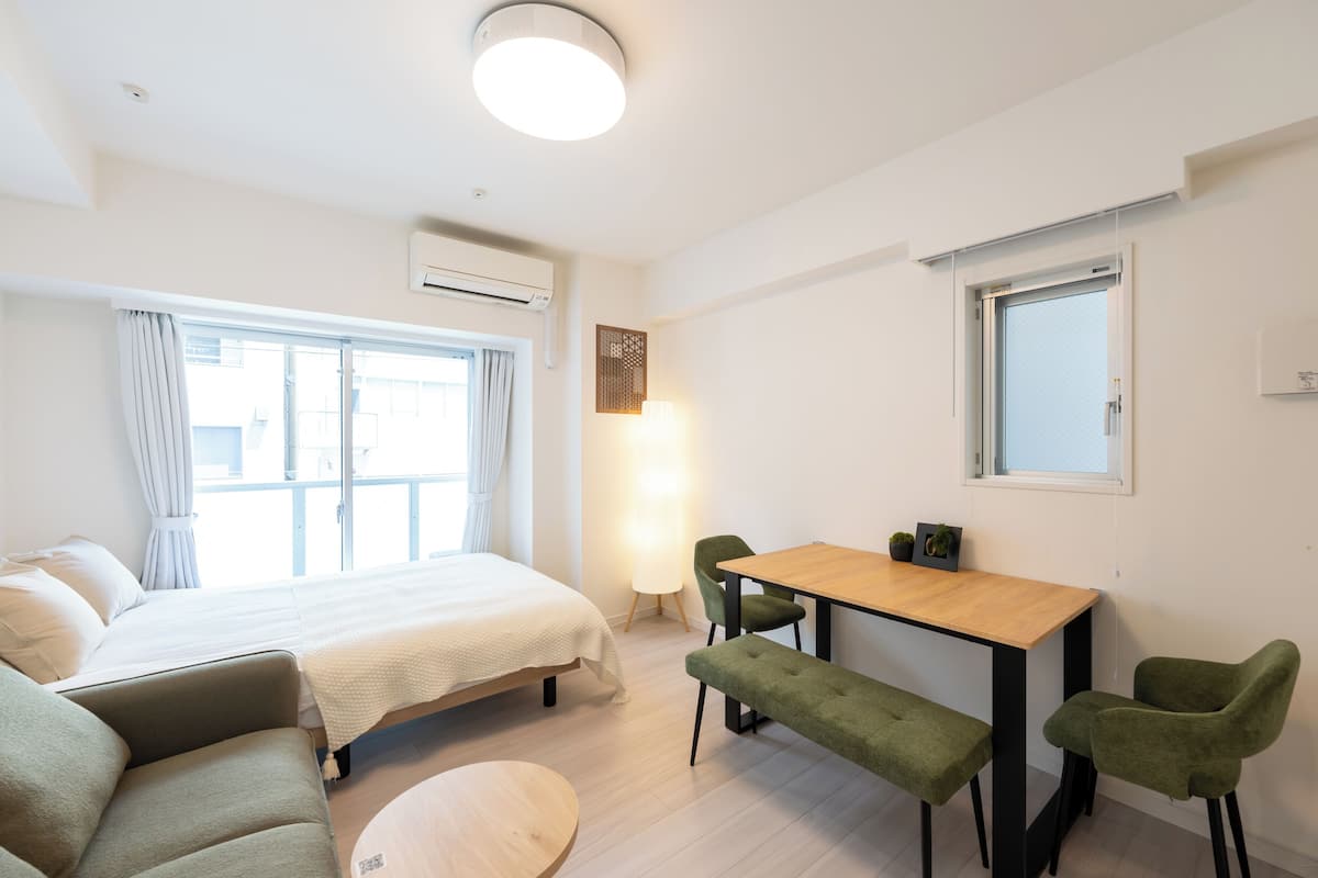 A modern, well-lit room with a bed, a wooden table, and green chairs.