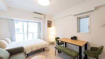 A modern, well-lit room with a bed, a wooden table, and green chairs.
