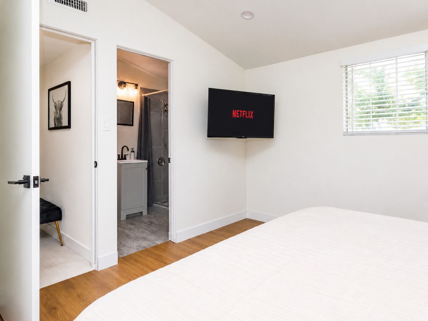 Ein Schlafzimmer mit einem Bett, einem an der Wand befestigten Fernseher und einem durch eine offene Tür einsehbaren Badezimmer.