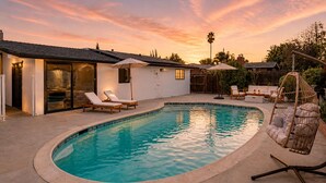 A swimming pool with lounge chairs and a hanging chair, surrounded by a house with a patio. - Spacious 4BR Home w/ Cozy Fireplace, Pool & Easy Access to LA Attractions (Calabasas)