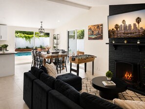 A modern living room with a black sofa, a dining area with a table and chairs, a pool, and a fireplace with a cityscape painting.
