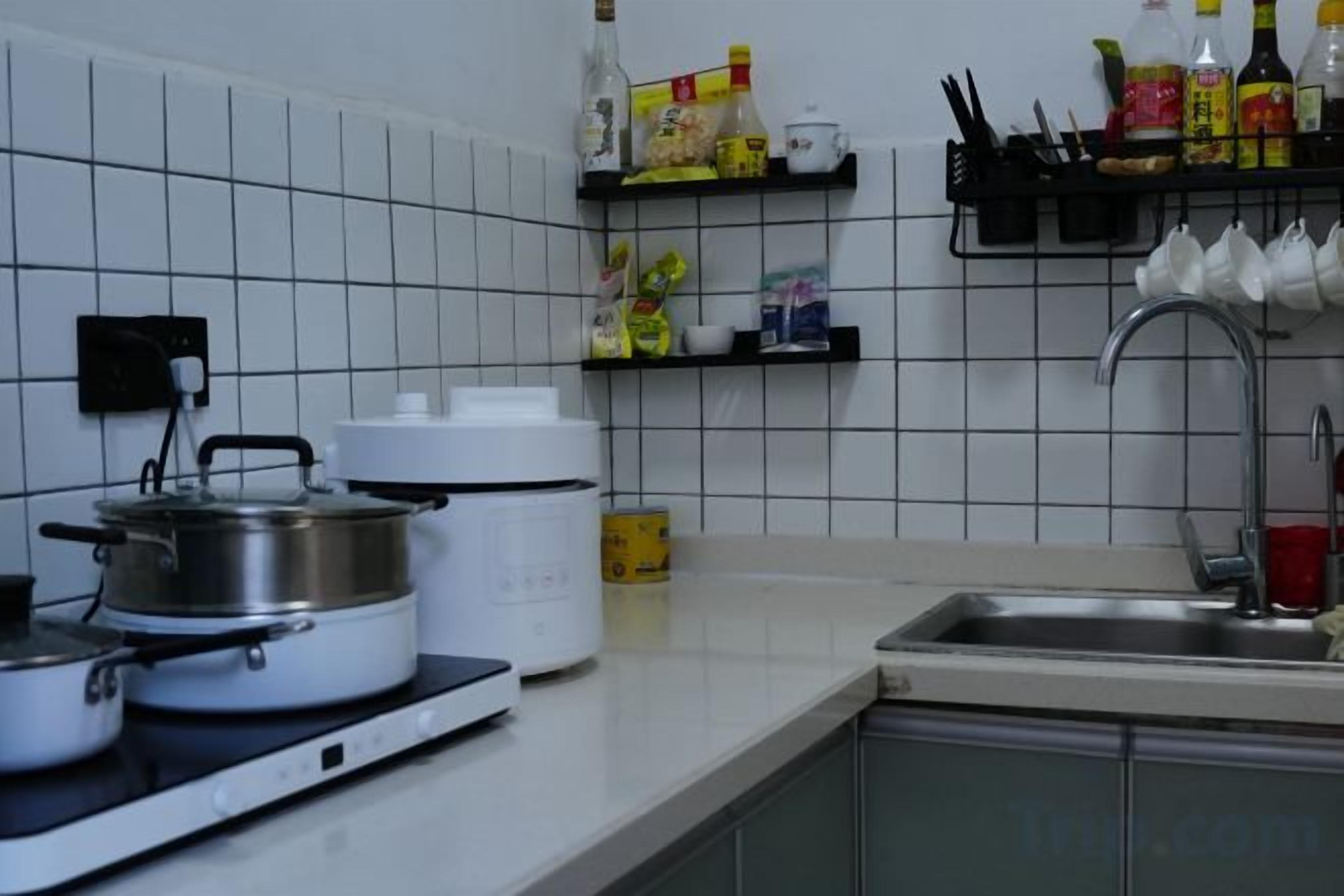 Una cocina con estufa, ollas, una cocedora de arroz y un fregadero.