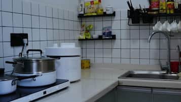 Una cocina con estufa, ollas, una cocedora de arroz y un fregadero.