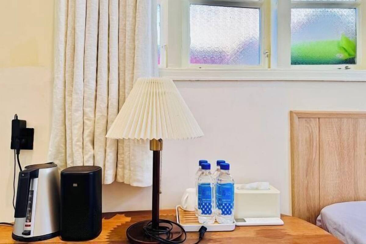 Une chambre d’hôtel équipée d’une table de chevet, d’une lampe, d’un haut-parleur, d’une bouteille d’eau et d’une boîte de mouchoirs.