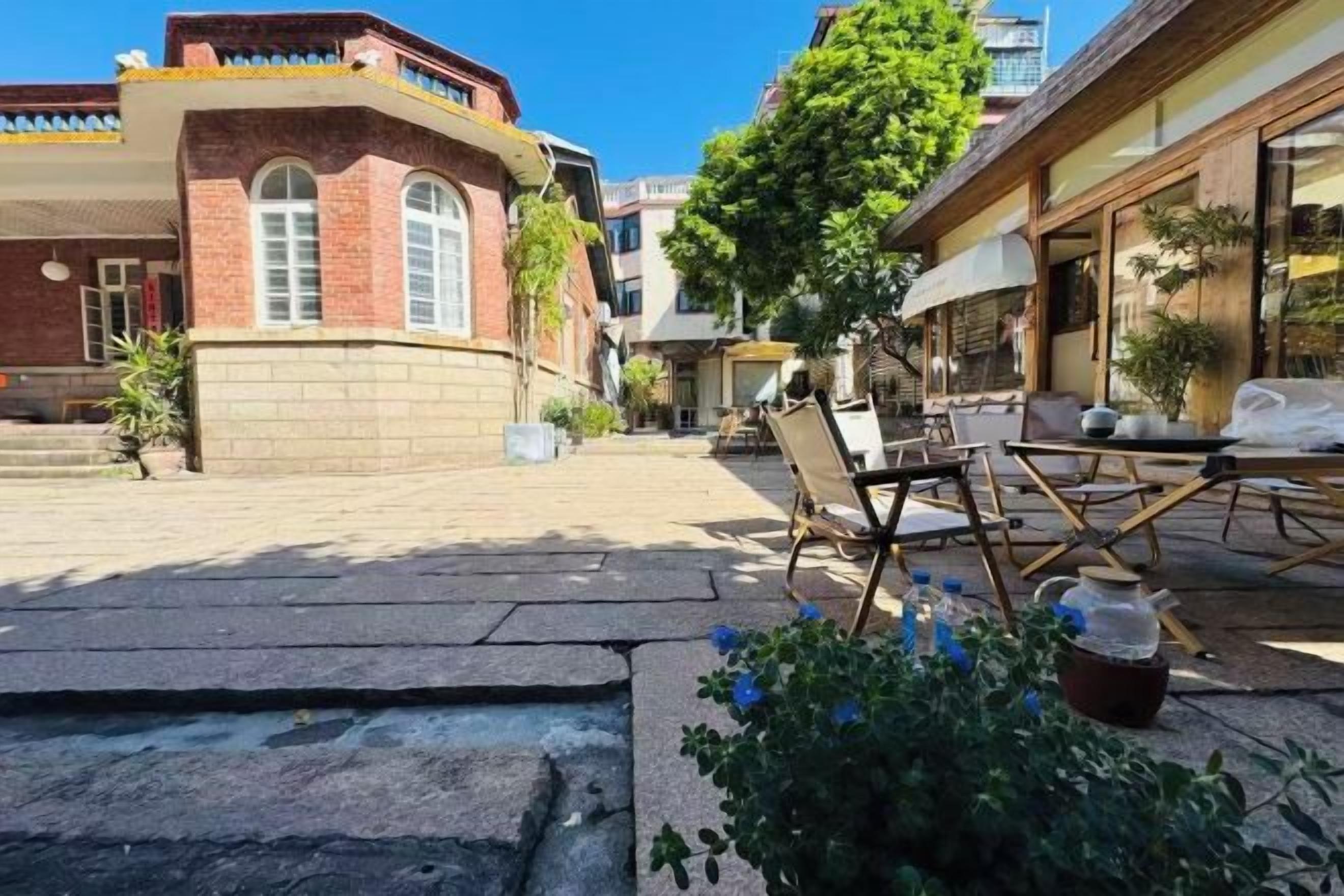 An outdoor seating area with tables and chairs, a stone pathway, and a building with a red brick facade.