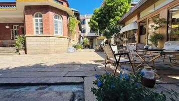 An outdoor seating area with tables and chairs, a stone pathway, and a building with a red brick facade.