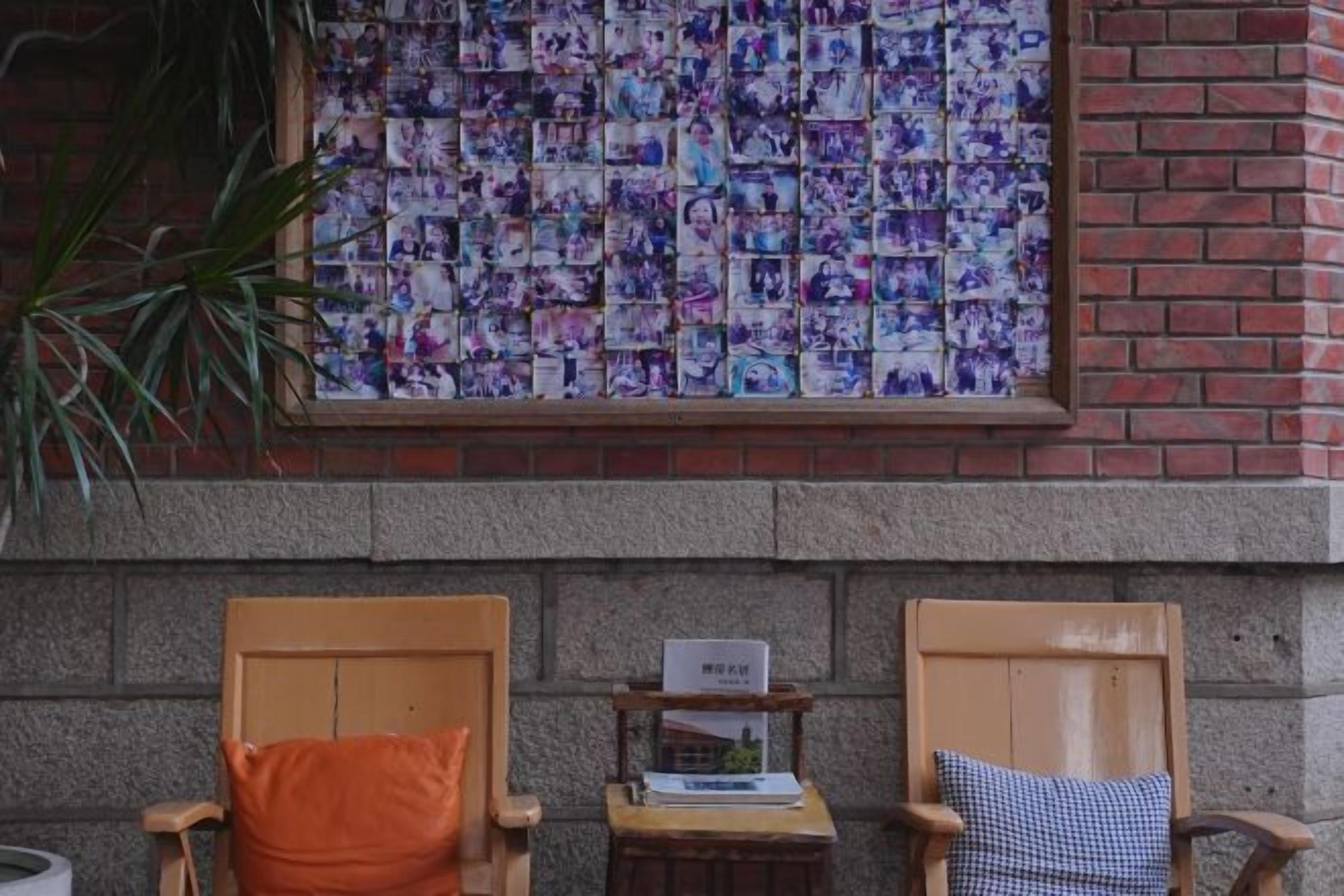 Dos sillas de madera con cojines, una mesita con un libro y una pared con un mosaico.