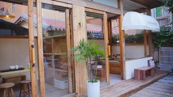 A wooden exterior with large glass doors, a potted plant, outdoor seating, and a white umbrella.