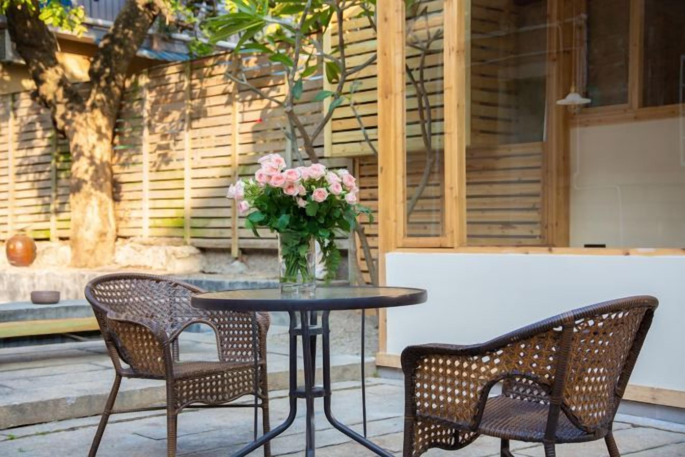 A patio with wicker chairs, a glass table, and a vase of flowers.