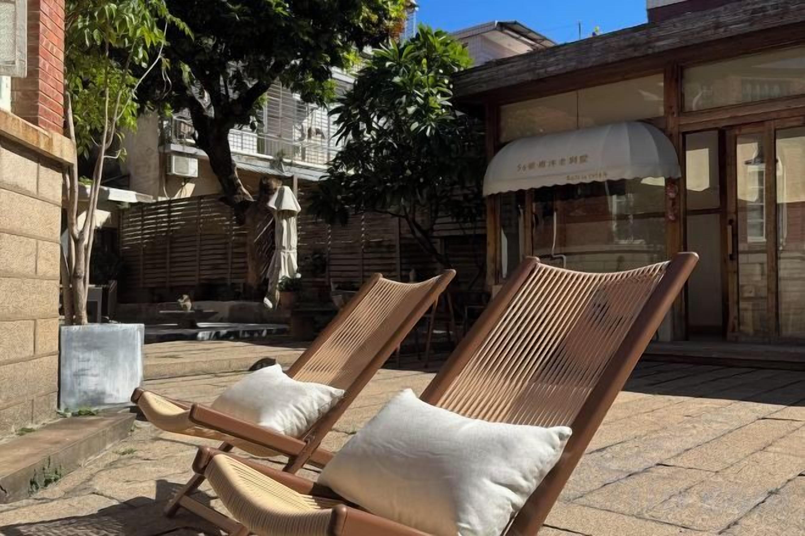 Two wicker lounge chairs with cushions, positioned on a paved patio with a building in the background.