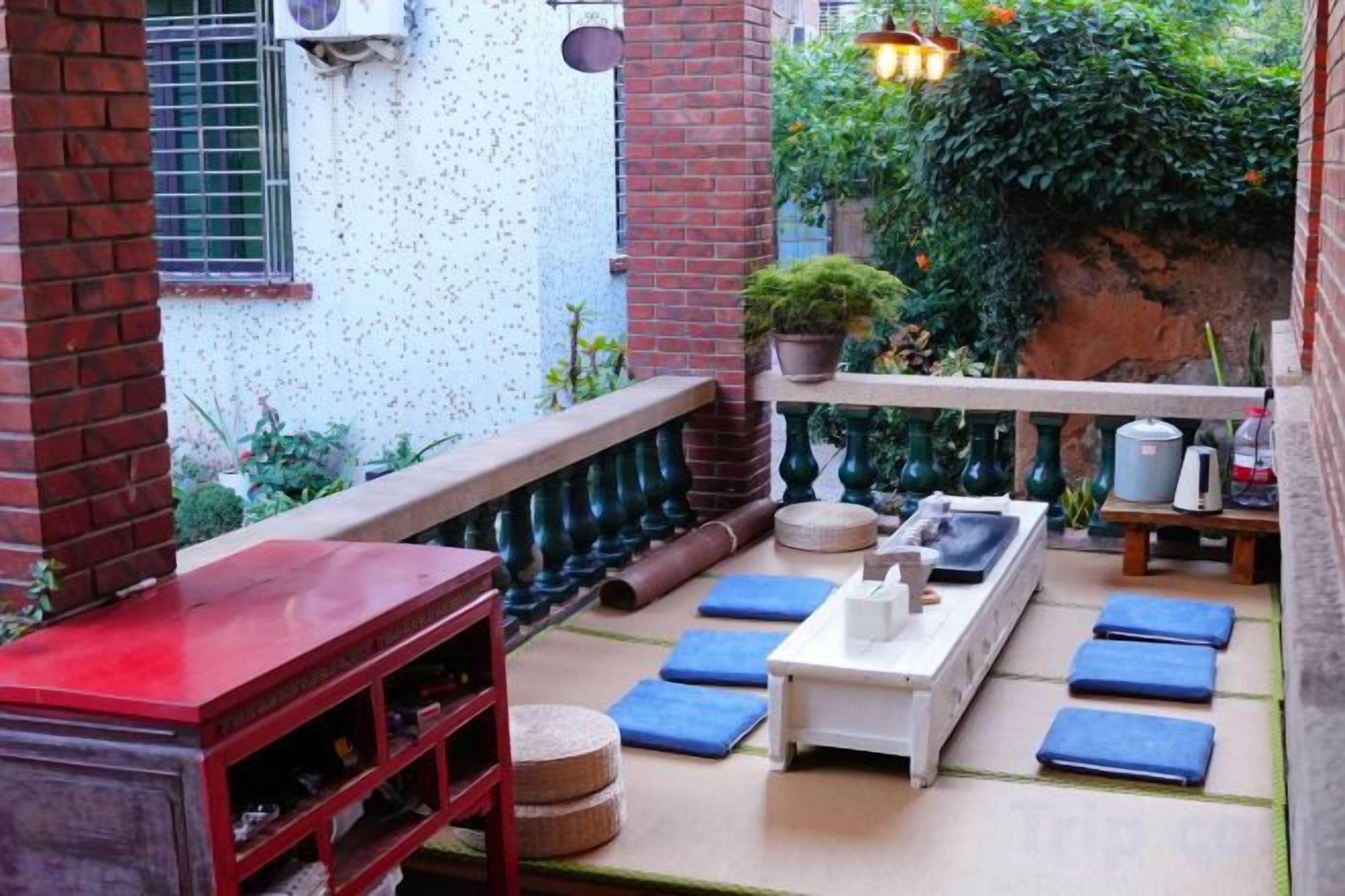 Un patio exterior con mesa de madera, cojines azules y pared de ladrillo.
