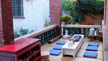 Un patio exterior con mesa de madera, cojines azules y pared de ladrillo.