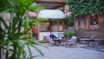 An outdoor seating area with tables and chairs, a covered kiosk, and a building with a stone facade.