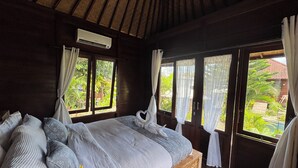 Une chambre avec un lit en bois, une fenêtre avec des rideaux et une vue sur la verdure.