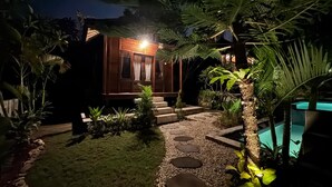 Une vue nocturne d’une maison à l’extérieur en bois, avec un chemin de pierre et une piscine.