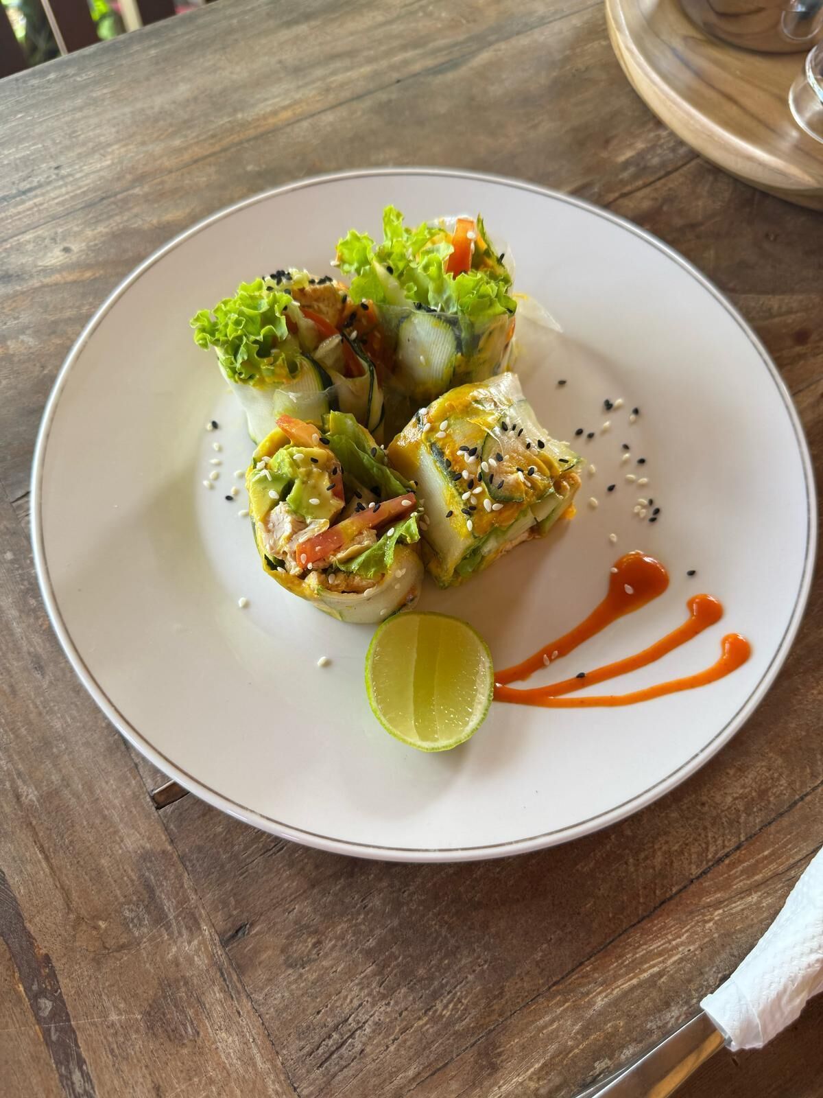 A plate with food items, a lime wedge, and a sauce on a wooden table.