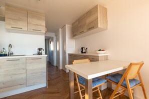 A modern kitchen with wooden cabinets, a white countertop, and a dining area with a white table and wooden chairs.